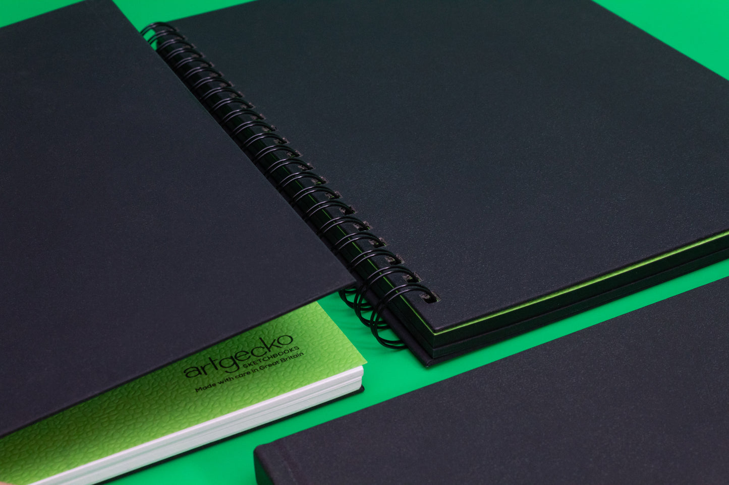 An image of three black covered Artgecko Sketchbooks with one cover open slightly to reveal a green cover sheet.