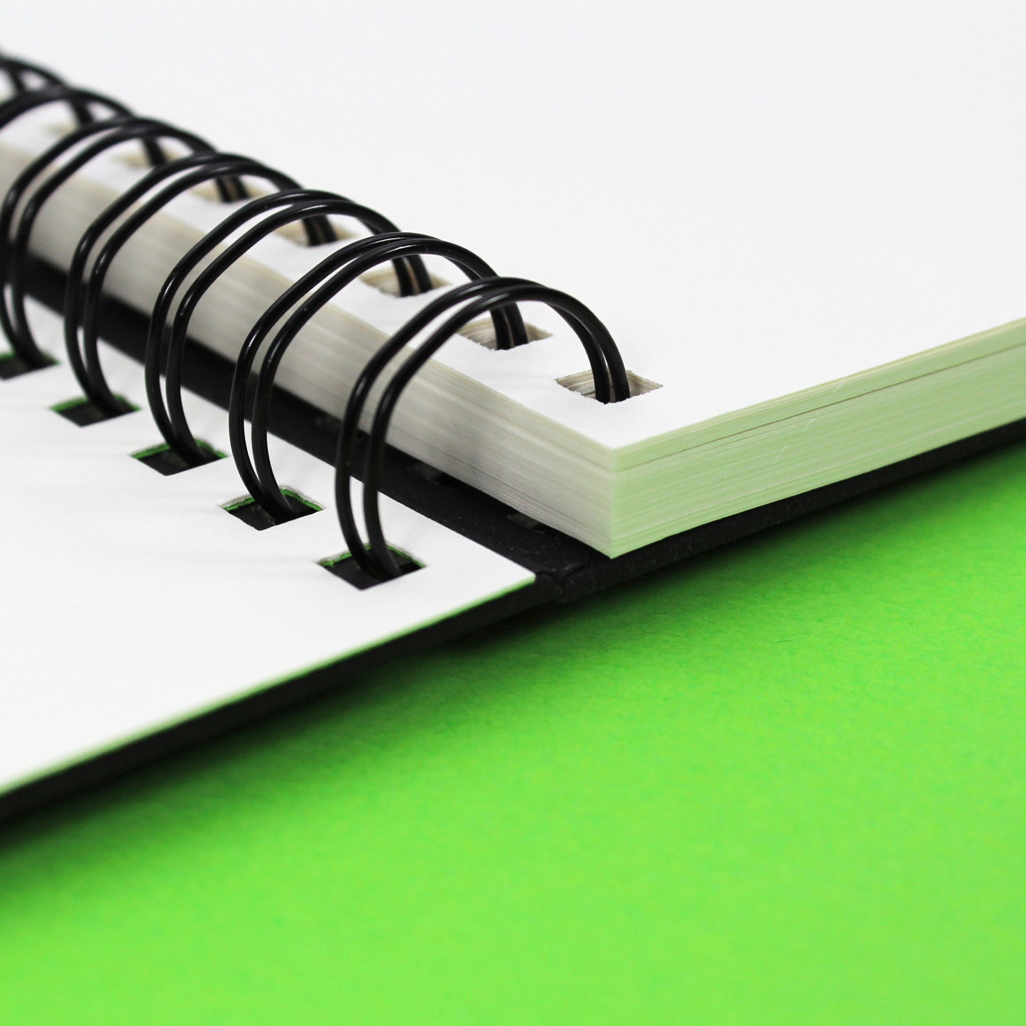 Close-up of a black all media sketchbook with white cartridge paper on green background with a black twin wire binding