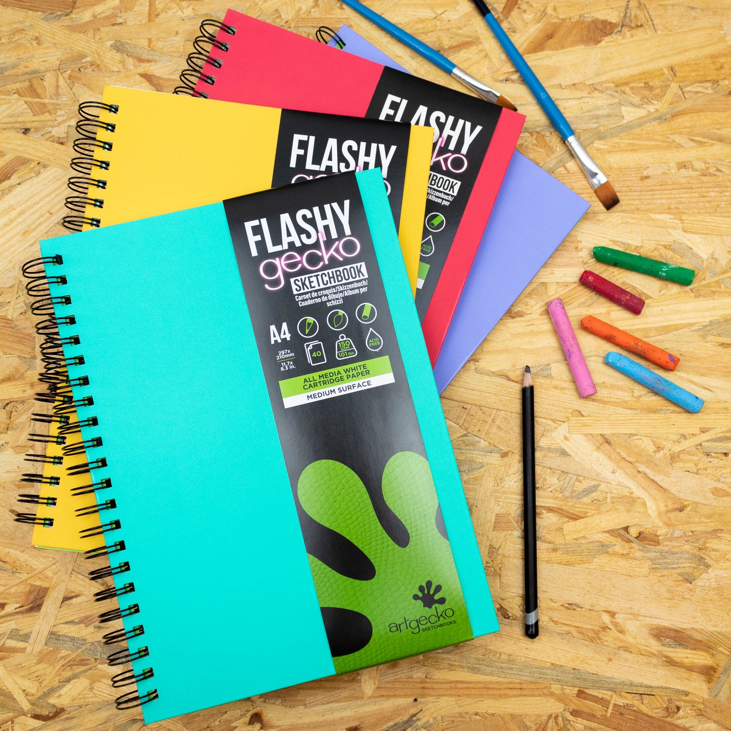 Colourful 'Flashy' sketchbooks with art supplies on a wooden surface by Artgecko