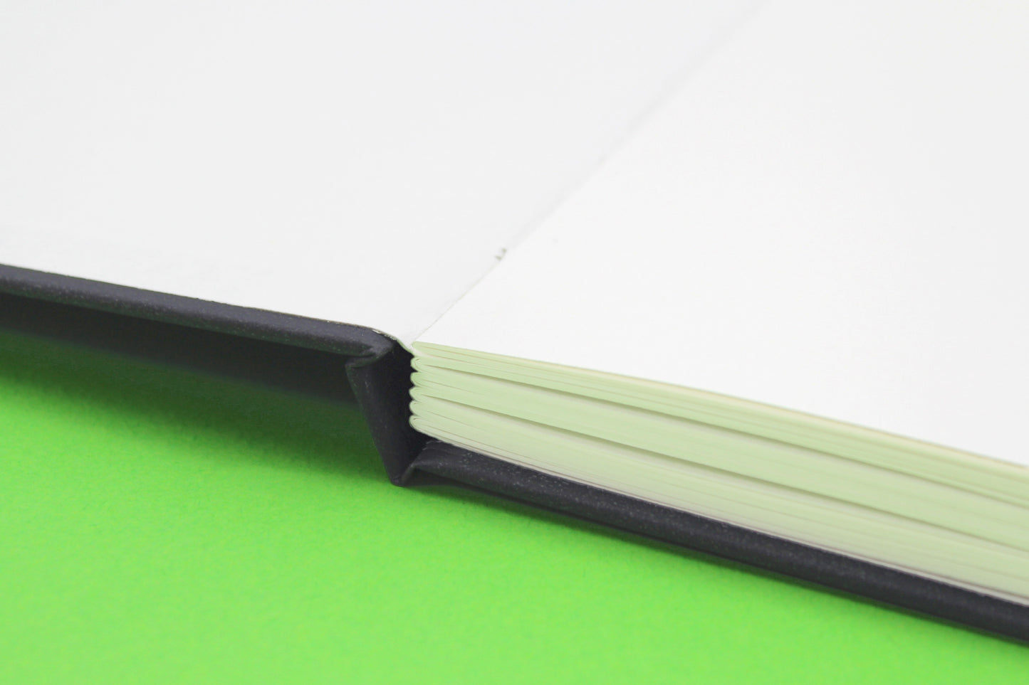 Close-up of a black all media sketchbook on green background with white cartridge paper with case bound binding
