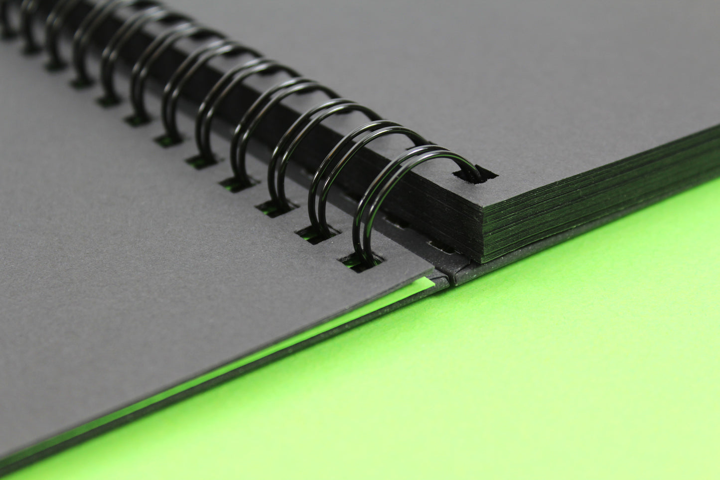 Close up of a 'Shady' Gecko sketchbook that is open to reveal the 200gsm black card inside and twin wire binding.